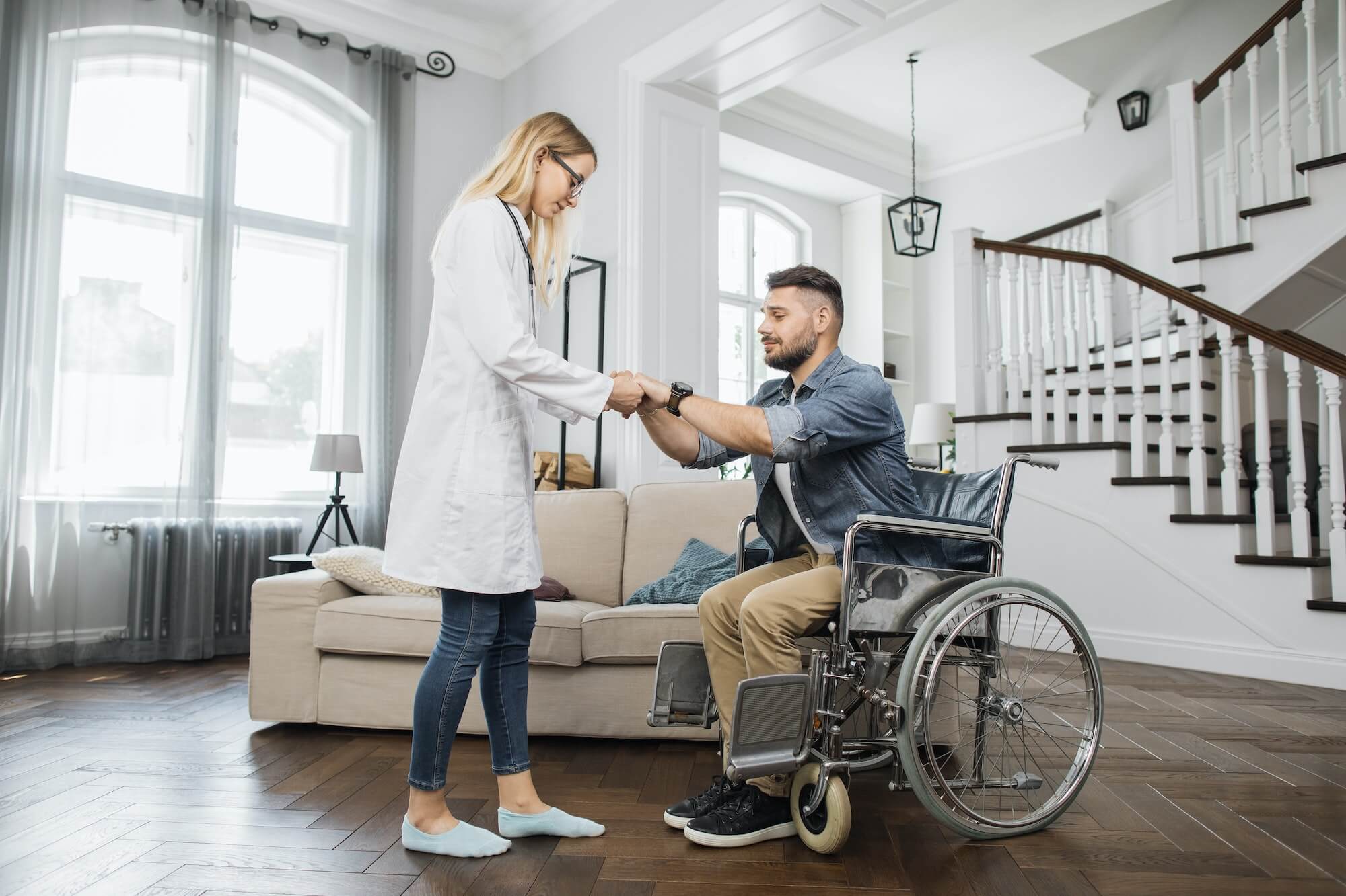 Therapist assisting man to stand up from wheelchair at home